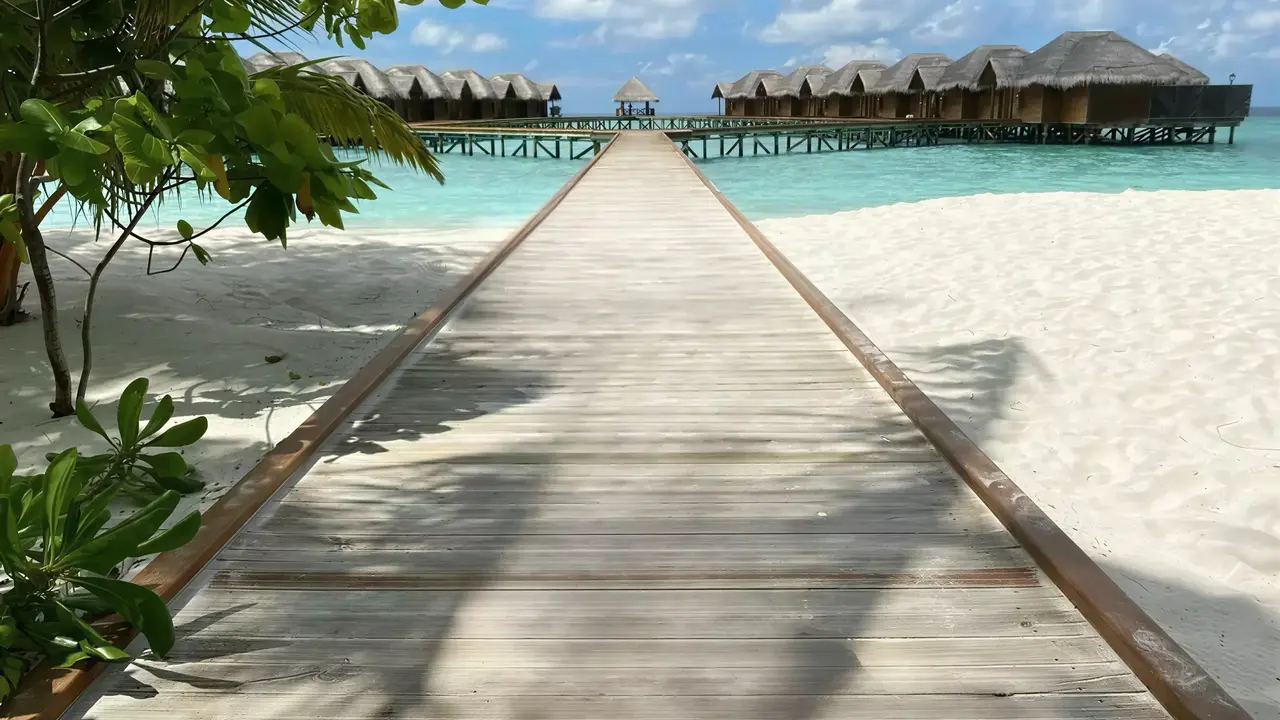 Drewniany pomost na białym piasku w Fihalhohi Island Resort
