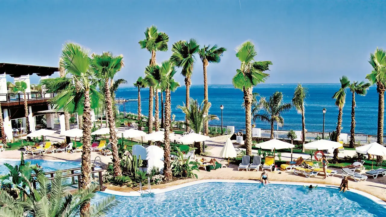Basen z leżakami i palmami w H10 Estepona Palace