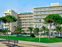 Budynek hotelu HTop Pineda Palace z trawnikiem i palmami