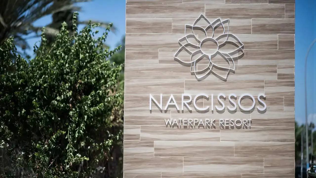 Szyld obiektu Narcissos Waterpark Resort na tle roślinności